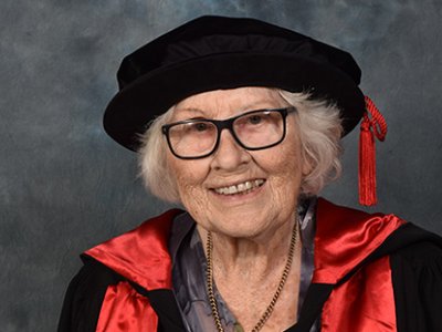 An older woman wearing a graduation gown and cap while smiling broadly