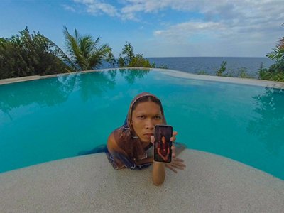A woman leaning onto the edge of a swimming pool, holding a mobile phone 