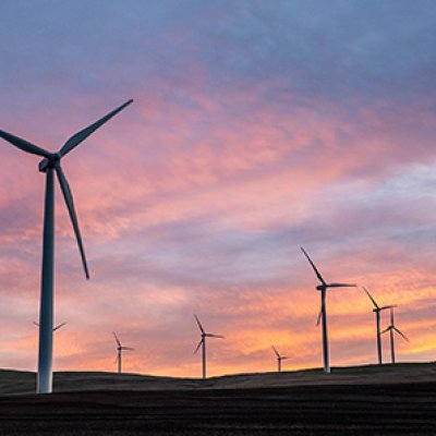 Ten wind turbines on grass hills at sunset