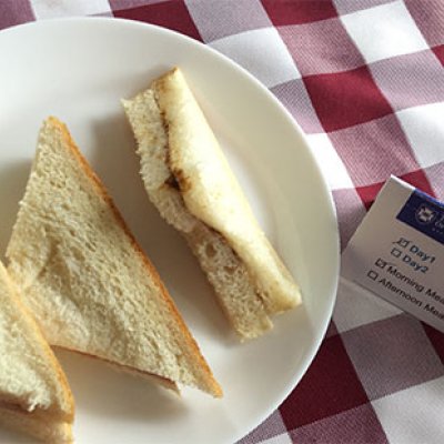 A plate of white, triangular sandwiches on a table with a red and white checkered table cloth 