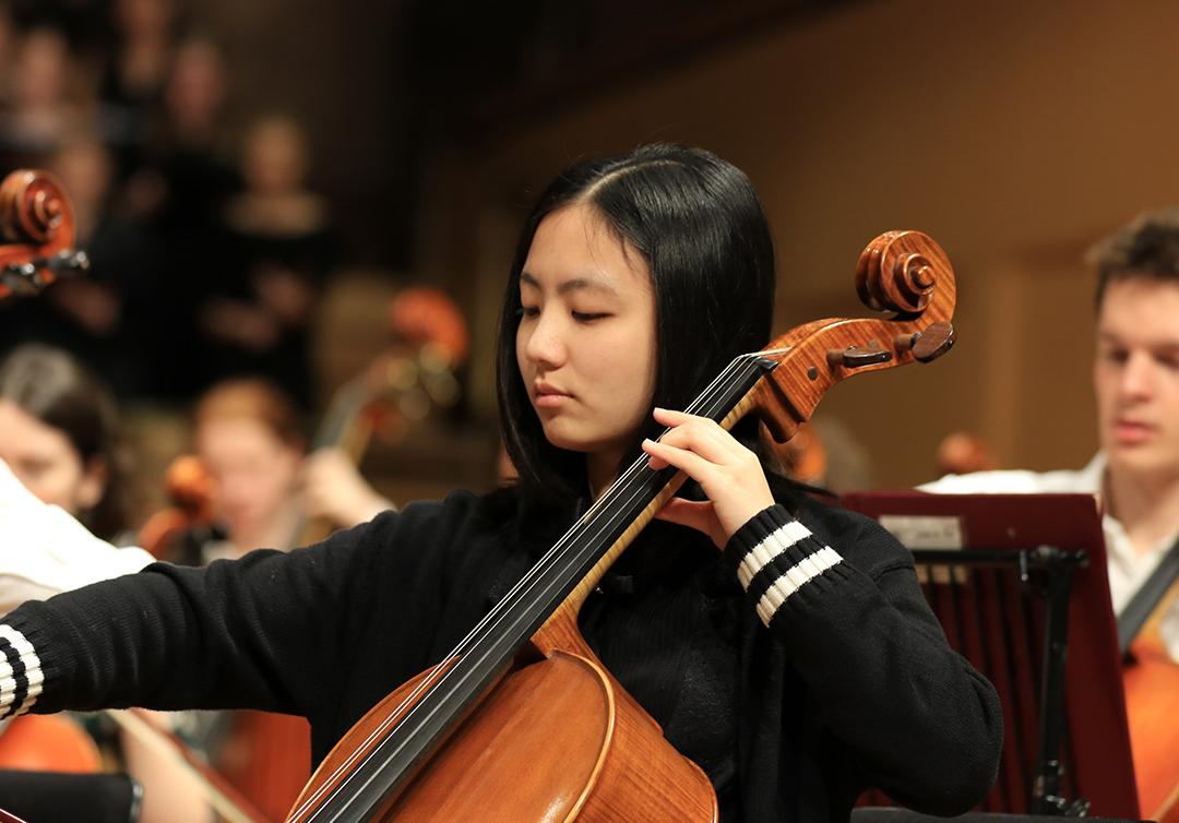 Student playing cello as part of an orchestra.